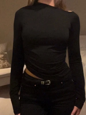 Svart långärmad asymmetrisk top - Säljer en svart långärmad topp med asymmetrisk halsringning och croppad passform. Toppen är figurnära och stretching.