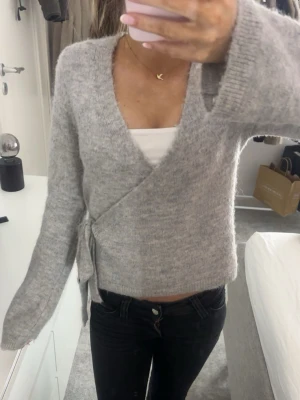 Grå omlottkofta med knyt i sidan - Supermysig grå stickad omlottkofta med knyt i sidan och v-ringad hals.🩶