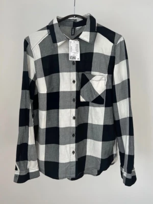 Rutig skjorta från H&M Divided - Säljer en ny rutig skjorta från H&M Divided i svart, grått och vitt. Skjortan har klassisk krage, bröstficka och knappar framtill 🖤