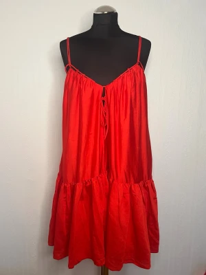 Röd sommarklänning från H&M XS - Snygg röd kort klänning från H&M i storlek XS. Klänningen har tunna axelband, v-ringning med snörning framtill och volang nedtill. Perfekt för varma dagar och enkel att styla med sneakers eller sandaler.oanvänd 