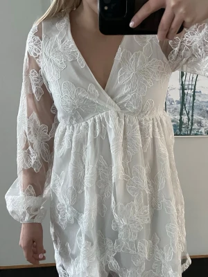 Vit kortklänning med spets - Vit kortklänning ifrån Gina tricot. Klänningen har v-ringning, omlott upptill och knyt i nacken. Aldrig använd, prislapp finns kvar.