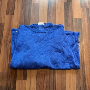 Blå stickad tröja med guldfärgade knappar - Blå stickad tröja i mjukt material med guldfärgade knappar på sidorna 💙✨Superfin statement-detalj som gör outfiten direkt mer intressant. Storlek: 42/44 Axelbredd: ca 50 cm Längd: ca 60 cm. 60% bomull, 40% viskos