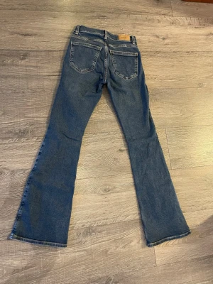 Blå bootcut jeans från Perfect Jeans - Säljer ett par klassiska blå bootcut jeans från Perfect Jeans i storlek 38. Jeansen har fem fickor, snygga kontrastsömmar och en riktigt schysst utsvängd passform. Materialet är slitstarkt jeans och färgen är en djup blå denim.