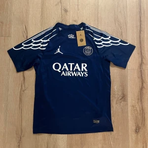 PSG x Jordan marinblå fotbollströja S - Marinblå PSG x Jordan fotbollströja i snabbtorkande polyester med vita detaljer och tryck. Unikt vingmönster på axlarna, klassisk rund hals och korta ärmar. Paris Saint-Germain-logga på bröstet och Jordan-logga. Snygg Qatar Airways-sponsor framtill.