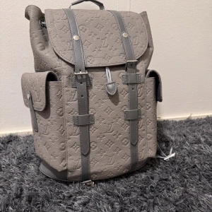 Grå Louis Vuitton ryggsäck i skinn - Snygg grå ryggsäck från Louis Vuitton i präglat skinn med klassiskt monogrammönster. Väskan har flera praktiska fack, justerbara axelremmar och detaljer i grått läder. Insidan har dragkedja och logopatch. ganska nytt skick