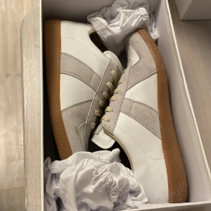 Maison Margiela GAT (äkthetsbevis finns) - Vita (german army trainers) från maison margiela i storlek 44. Köpta i maj 2025! ✅Det finns tecken på användning (fläck på högra tån och sulan har några markeringar från vanlig användning) ingen skada alls och fläcken går säkert att få bort. Allt og följer med vid köp, äkthetsbevis, boxen, dustbags. ✅jag är öppen för prisförslag ✅