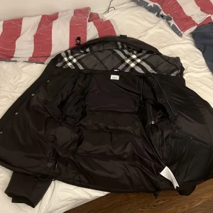 Svart Burberry dunjacka med rutig foder - Skriv med mig innan ni köper Säljer en svart dunjacka från Burberry London England med klassiskt rutigt foder i grått, vitt och svart. Jackan har dragkedja, långa ärmar och flera praktiska fickor. Perfekt för kalla dagar med sin tjocka och quiltade design.