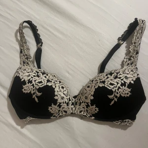 Svart intimissimi gioia pretty flowers super push up bh 75c - Säljer en intimissimi super push up gioia flowers bh i storlek 75c. Den har snygga vita spetsdetaljer och blommigt broderi över kuporna och axelbanden. Bh-n har v-ringad form och med justerbara band. Perfekt för dig som gillar en elegant och feminin stil.