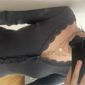 Grå ribbad långärmad topp med spets - Säljer en grå långärmad topp med ribbad struktur och snygga spetsdetaljer längs v-ringningen och nederkanten. Toppen har knappar framtill och sitter tight. Perfekt för dig som gillar stilrena och feminina plagg.