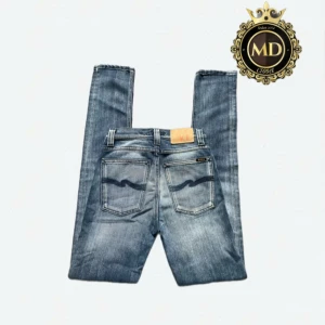  Nudie Jeans - Säljer ett par blå jeans från Nudie Jeans med klassisk femficksdesign och snygga slitningar. Jeansen har mörkblå broderade detaljer på bakfickorna och en läderpatch i midjan. Modellen är smal och sitter tajt längs benen. Perfekt för dig som gillar en stilren och modern look. Byxorna är i mycket bra skick. Skirv vid frågor eller mer bilder!⚜️