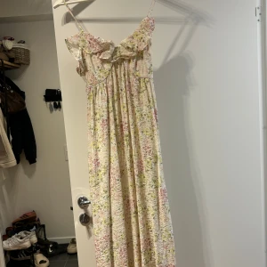 Blommig långklänning med volang - Säljer en romantisk långklänning med blommigt mönster i ljusa toner. Klänningen har smala axelband, volang upptill och en luftig passform som ger en skön känsla. Perfekt för varma dagar och somriga tillfällen.