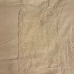 Vit spetslinne - Säljer en superfin vit linnetopp i spets med blommigt mönster. Toppen är ärmlös och har breda axelband med spetsdetaljer. Linnet är från Nelly. Använt få gånger!