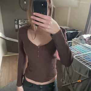 Brun ribbad långärmad topp från Pieces - Säljer en brun långärmad topp från Pieces i ribbad bomull. Toppen har v-ringning med små knappar framtill och är croppad i modellen. 