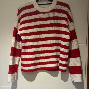 Randig stickad tröja från Monki - Riktigt snygg stickad tröja från Monki med breda röda och vita ränder. Tröjan har rund halsringning och långa ärmar. Materialet är en mix av polyester, akryl och ull som gör den både mjuk och varm. 