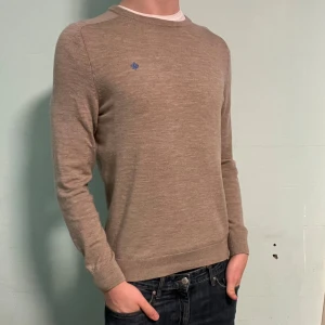 Beige merinoullströja från Morris - Snygg beige stickad tröja från Morris i 100% merinoull. Klassisk rund halsringning och diskret blå logga broderad på bröstet.  Bara att höra av dig om du har några frågor. Allt gott deluxe garderoben🤩