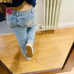 One Dilemma jeans med stjärnor & nitar - Blå jeans från One Dilemma med raka ben, silverfärgade nitar i midjan och längs bensluten samt glittriga stjärnor på bakfickorna. Tuff rosa patch bak i midjan. Perfekta för dig som vill sticka ut med coola detaljer och unik look.