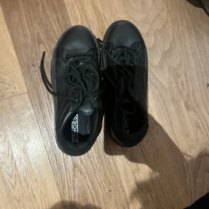 Svarta sneakers från Shoeshine - Svarta sneakers med rund tå och platt sula från Shoeshine. Skorna har snörning och är tillverkade i syntetmaterial med en stilren, monokrom look. Perfekta för dig som gillar minimalistisk stil och vill ha ett par klassiska svarta sneakers.