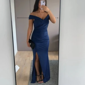 Marinblå balklänning med slits - Säljer en elegant marinblå balklänning med offshoulder och snygg v-ringning. Klänningen har draperade detaljer och en hög slits framtill som ger en extra touch. Använd en gång på min balkväll. 
