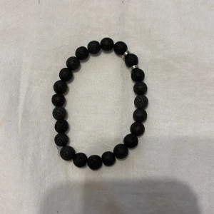 Svart armband med lavapärlor - Stilrent armband med svarta lavapärlor och små silvriga detaljer. Pärlorna är runda och har en cool, porös yta som ger en unik känsla. Perfekt accessoar för dig som gillar minimalistisk och modern stil.
