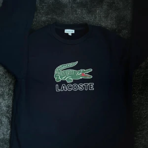 Mörkblå sweatshirt från Lacoste - Snygg mörkblå sweatshirt från Lacoste med det klassiska gröna krokodilmotivet och stor logga framtill. 