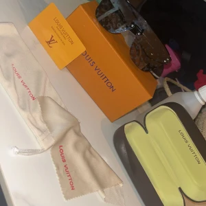 Louis Vuitton monogram solglasögon - Säljer ett par svarta Louis Vuitton solglasögon med ikoniskt monogrammönster över hela linsen. Modellen har en bred, futuristisk form och kommer med originalfodral, putsduk och box. Perfekt för dig som vill sticka ut med lyxig designerstil.