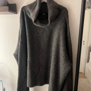 Mörkgrå polotröja från Bik Bok - Mysig och oversized mörkgrå polotröja från Bik Bok med grov ribbad stickning. Tröjan har en bred och hög polokrage samt långa ärmar. Perfekt för kalla dagar och enkel att styla med jeans eller leggings.