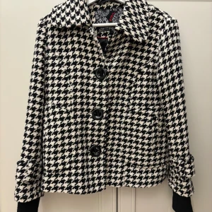 Rutig kavajjacka från Zoul, storlek 36 - Snygg svartvit rutig kavajjacka från Zoul i storlek 36. Jackan har stora svarta knappar framtill, klassisk krage och långa ärmar med knappdetalj vid mudden. Materialet är grovvävt och ger en cool, trendig vibe. Perfekt för dig som gillar statement-plagg.