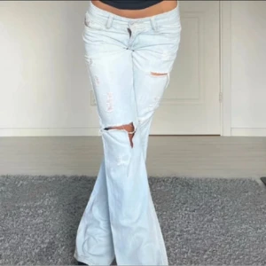 Ljusblå bootcut jeans med slitningar - Säljer ett par ljusblå jeans med bootcut-modell och snygga slitningar på benen. Jeansen har låg midja och klassiska fem fickor. Perfekta för dig som gillar en avslappnad och trendig stil. Midjemåttet 37. Innerbensmåttet 79