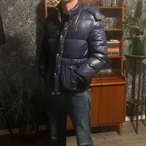Mörkblå pufferjacka Polo Ralph Lauren Barn XL(xs-s herr) - Säljer en mörkblå pufferjacka från Polo Ralph Lauren i storlek barn XL(xs-s i herr). Jackan har huva, guldfärgade knappar, två stora fickor fram och röd Polo-logga på bröstet. Materialet är glansigt och fylligt, perfekt för kalla dagar. Snygg och klassisk look. obs den har ett väldigt litet hål på framsidan som nästan är helt osynligt om man inte kollar väldigt nära eller känner direkt på det. Priset är ej hugget i sten! kom med bud