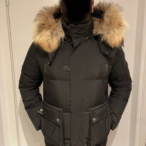 Svart dunjacka med päls från Cedrico - Säljer min  svart vinterjacka  från Cedrico med stor fluffig päls runt huvan. Jackan har flera fickor med tryckknappar, dragkedja och hög krage. Perfekt för kalla dagar och riktigt snygg streetstil jackan har aldrig använts. 