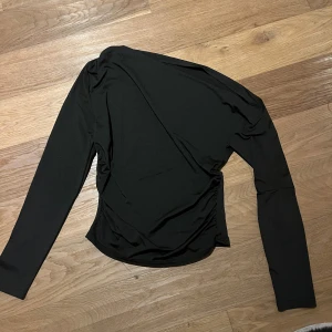 Svart oneshoulder långärmad topp - Säljer en svart långärmad topp med oneshoulder-design. Snygg asymmetrisk form som ger en cool och modern vibe. Materialet är mjukt och stretchigt, perfekt för att skapa en stilren look. Passar dig som gillar minimalistiska plagg med en twist.