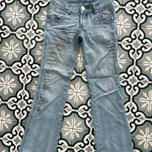 Ljusblå bootcut jeans med slitningar - Snygga ljusblå jeans från Foxy i bootcut-modell med slitna detaljer framtill och nitar vid fickan. Jeansen har klassisk femficksdesign och är tillverkade i denim.