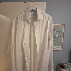 Vit slim fit skjorta från Eton - Vit skjorta från Eton i slim fit med klassisk krage och snygga knappar. Insidan av kragen har ett diskret ljusblått mönster som ger en fräsch touch. Skjortan är långärmad och tillverkad i mjuk bomull, perfekt för dig som gillar stilrena och cleana plagg.