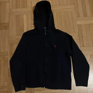 Ralph lauren tröja - Modern Ralph lauren tröja köpt på nk 100% äkta. Tröjan har huva, långa ärmar och två fickor framtill. Tillverkad i mjuk bomull som är skön att ha på sig.