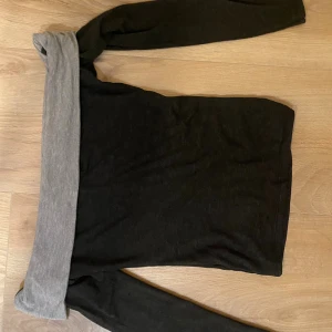 Svart offshoulder tröja med grå kant - Säljer en svart offshoulder tröja från design by si Tröjan har långa ärmar och är figurnära i modellen. Perfekt att styla med jeans för en cool och avslappnad look.