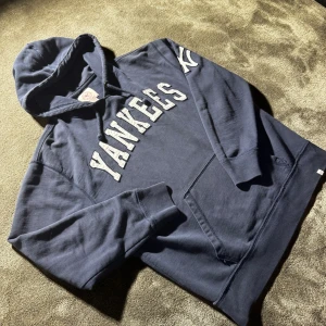 Vintage Yankees hoodie 🗽 - Säljer en Vintqge hoodie från med Yankees-tryck i vitt framtill och på ärmen. Tröjan har huva med snörning och en stor magficka. Tillverkad i 100% bomull, perfekt för dig som gillar sportig och avslappnad stil.