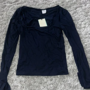 Mörkblå långärmad topp från Gina Tricot - Säljer en mörkblå långärmad topp från Gina Tricot, Elevated Basics. Toppen har en djupare rundad halsringning och är gjord i ett mjukt, stretchigt material som känns skönt mot huden. Perfekt för dig som gillar stilrena och enkla plagg med modern passform. Helt ny med prislapp aldrig använd