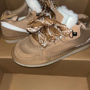 Beige sneakers med pälsfoder - Snygga beige sneakers med grova, mönstrade snören i brunt och vitt. Skorna har pälsfoder på insidan för extra värme och komfort, samt detaljer i mocka och textil. Rund tå och platt sula gör dem perfekta för en chill stil under kalla dagar.