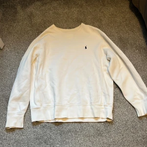 Vit sweatshirt från Polo Ralph Lauren - Vit sweatshirt från Polo Ralph Lauren med klassisk rund hals och broderad marinblå logga på bröstet. Tröjan är tillverkad i bomull och polyester för en mjuk och skön känsla. Perfekt för en clean och stilren look. Kan passa en M också. Original pris 2195kr