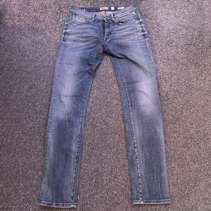 Replay Anbass jeans ljusblå 30/32 - Snygga Replay Anbass jeans i ljusblå tvätt med klassisk femficksdesign och broderade detaljer på bakfickorna. Modellen har smal passform och raka ben, tillverkade i mjukt jeanstyg med diskret slitning för en cool look.