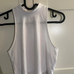 Vit croppad linnetopp från Madlady - Säljer en vit croppad linnetopp från Madlady med hög hals och ärmlös design. Toppen är slät och har en clean look, perfekt för att styla med jeans eller kjol. Materialet är mjukt och stretchigt polyester som sitter skönt.