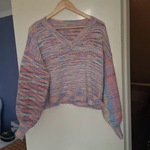 Pastellfärgad stickad tröja v-ringad - Supermysig stickad tröja i pastellfärger med v-ringning och ballongärmar. Tröjan har en loose passform och är perfekt för dig som gillar färg och vill ha något unikt. Färgerna går i lila, rosa, blått och gult. Perfekt att slänga på sig under kyliga dagar.