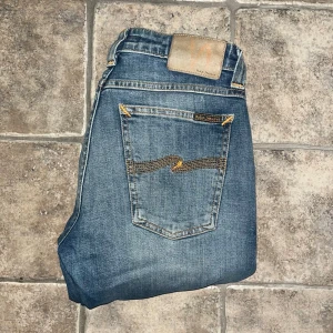 Nudie Jeans  - Snygga blå jeans från Nudie Jeans i modellen Skinny Sam. Jeansen har klassisk femficksdesign, gul kontrastsöm och broderad bakficka. Tillverkade i stretchig denim av bomull och elastan för en bekväm passform. Midja 36cm, längd 103cm.  Ifall det inte finns någon bild i annonsen där jag bär plaggen jag säljer så är det för att jag ej kan ha storleken heller passformen, så kolla måtten för storlek och googla på modellnamnet för passform 😉 s4