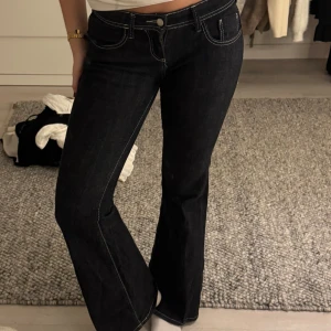 Mörkblå bootcut jeans  - Snygga mörkblå jeans med bootcut-modell och tydliga vita kontrastsömmar. Klassisk femficksdesign och låg midja. Jeansen är tillverkade i ett stadigt denimtyg som ger en schysst passform och markerar siluetten på ett stilrent sätt.
