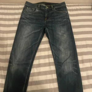 Blå jeans från Tiger of Sweden - Snygga blå jeans från Tiger of Sweden med klassisk femficksdesign och diskreta slitningar framtill. Jeansen har raka ben och normal passform, tillverkade i slitstarkt denim med snygga kontrastsömmar. Perfekta för en stilren och avslappnad look.