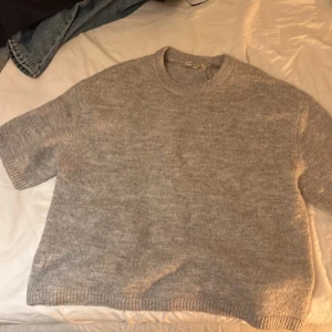 Grå stickad tröja Gina Tricot - Mysig grå stickad tröja från Gina Tricot i storlek S. Tröjan har korta ärmar, rund hals och ribbade kanter vid hals och nederkant. Perfekt för dig som gillar en enkel och chill stil med lite loose passform.