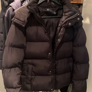 Svart pufferjacka från ASOS DESIGN - Säljer en svart pufferjacka från ASOS DESIGN i storlek 2XS. Jackan har en hög krage, dragkedja och tryckknappar framtill samt två sidofickor. Den är vadderad och har en klassisk, boxig passform som är perfekt för kalla dagar. Modellen är 186, 70 kg. 