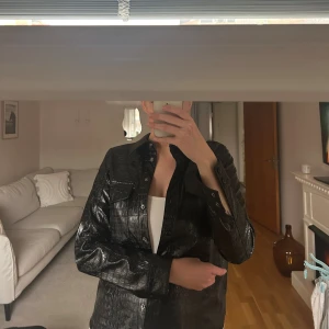 Svart skinn Carin Wester - Säljer en svart overshirt från Carin Wester i coolt croco-mönstrat skinnimitation. Jackan har knappar hela vägen, två bröstfickor med lock och klassisk krage. Perfekt att styla lager på lager för en edgy vibe.