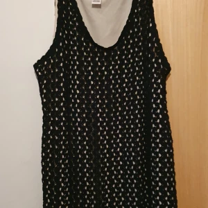 Klänning - Svart kortklänning från Motherhood Maternity i storlek L. Klänningen har ett snyggt hålmönster och är ärmlös med rund hals. Medföljer ett vitt knytband i midjan för extra stil. Perfekt för dig som gillar en loose passform och vill ha något bekvämt och trendigt.