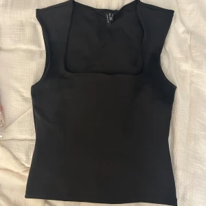 Svart ärmlös topp från Vero Moda - Säljer en svart, stilren ärmlös topp från Vero Moda. Toppen har en fyrkantig ringning och är figurnära i modellen. Perfekt att matcha med jeans eller kjol för en clean look.